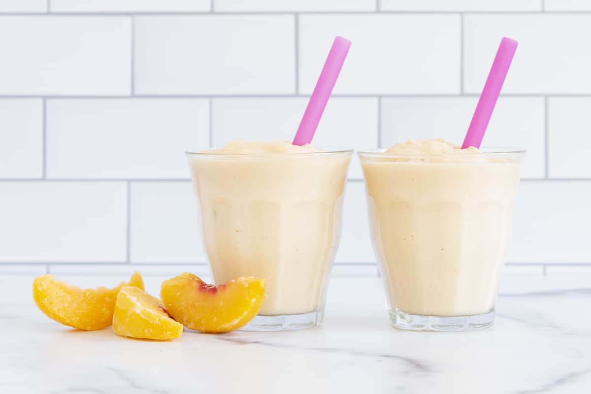 Peach smoothie in two glasses with peaches on side