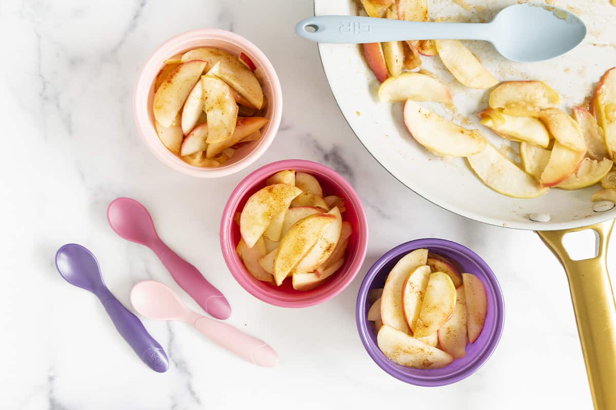 cinnamon apples in three bowls and pan with spoons.