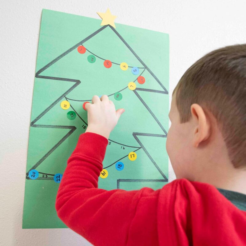 A child places a dot sticker onto a green construction paper Christmas tree in a math activity.