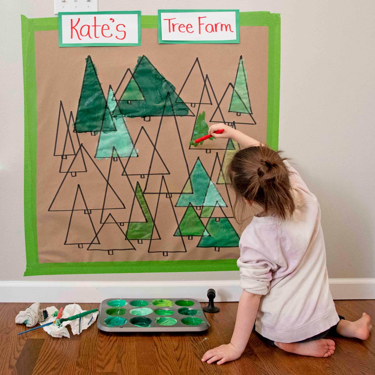 A child reaches up and paints one of several green triangles on a brown piece of paper.