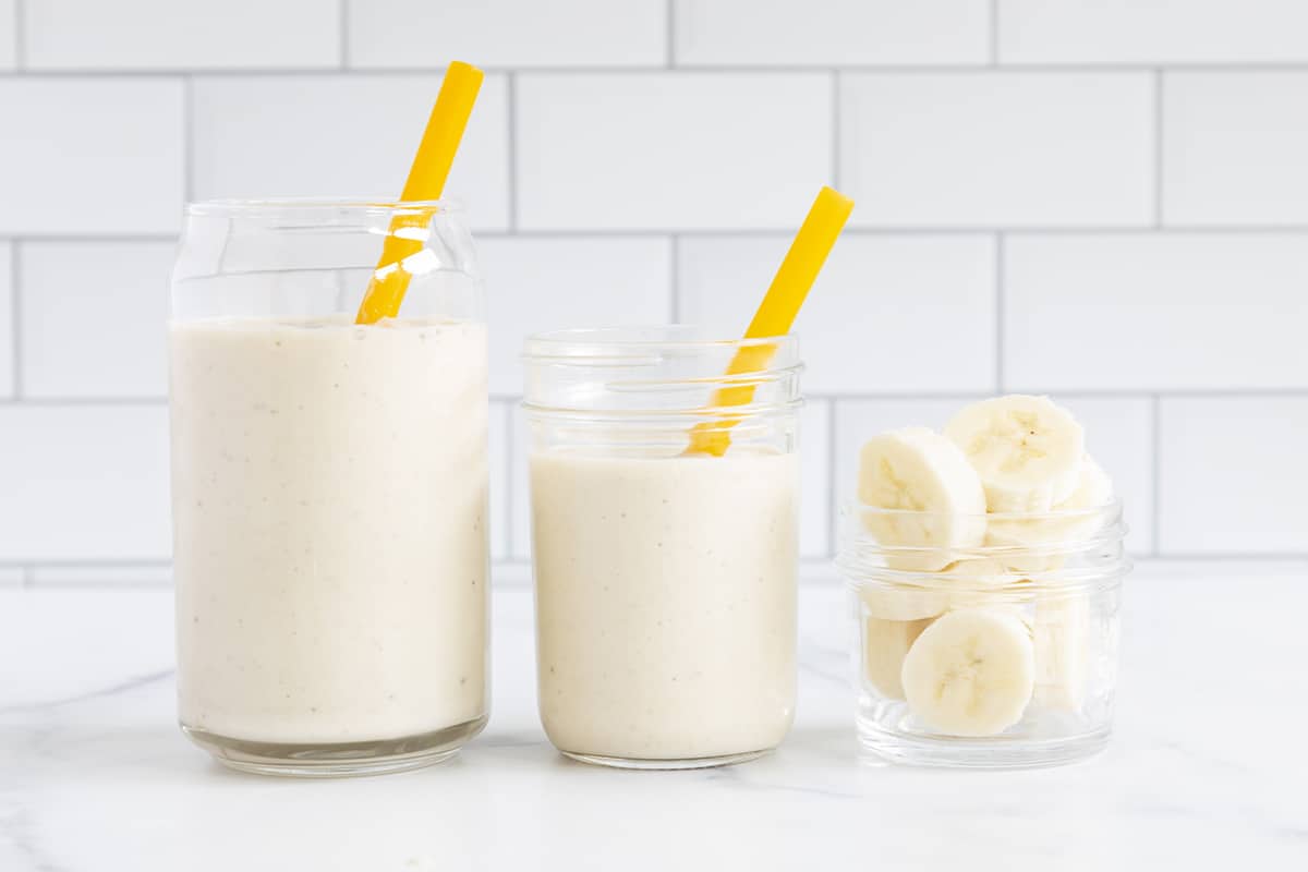 banana smoothie in two cups with sliced bananas in glass.
